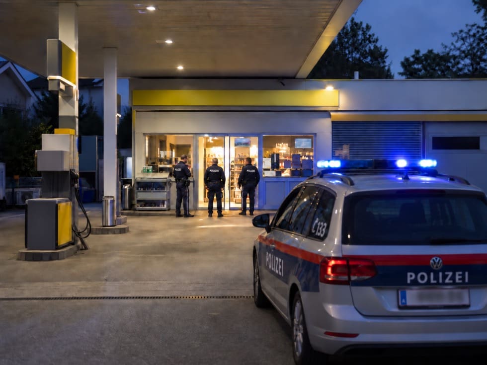 Polizeibeamte stehen vor einer beleuchteten Tankstelle mit einem Streifenwagen und Blaulicht bei Nacht