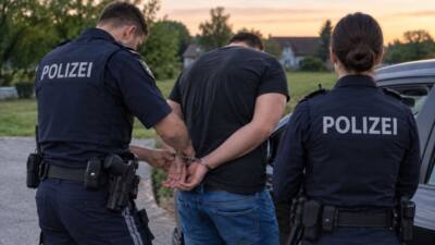 Zwei Polizeibeamte in Uniform legen einem Mann Handschellen hinter dem Rücken an.