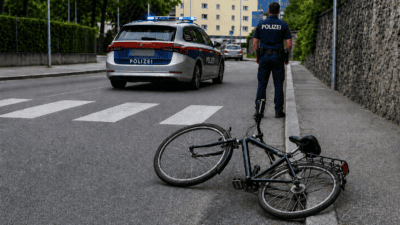 Polizeiauto mit Blaulicht und Polizist neben einem gestürzten Fahrrad auf der Straße