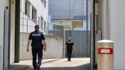 Zwei Polizisten in Uniform gehen von hinten durch eine große Tür in einen Industriebereich.