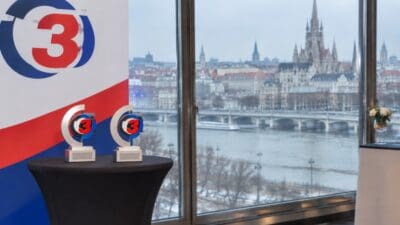 Zwei Trophäen mit dem Logo von Ö3 auf einem schwarzen Tisch vor einem großen Fenster mit Stadtpanorama
