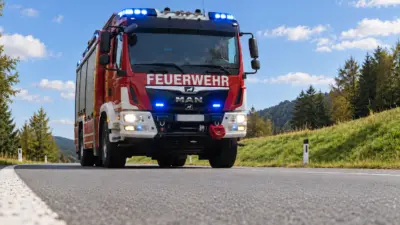 Rotes Feuerwehrfahrzeug mit Blaulicht auf einer Landstraße in hügeliger Landschaft