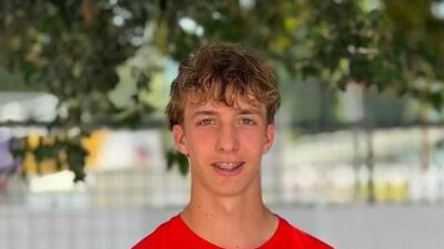 Junger Mann mit braunem Haar in rotem T-Shirt lächelt mit Zahnspange in die Kamera