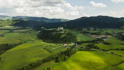Luftaufnahme der Burg Hochosterwitz auf einem bewaldeten Hügel inmitten grüner Felder und Wiesen.