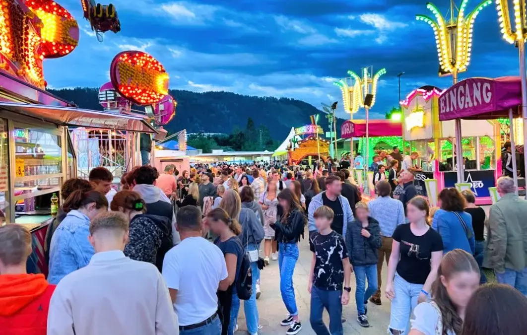 Besucher gehen zwischen beleuchteten Fahrgeschäften und Buden über den St. Veiter Wiesenmarkt.