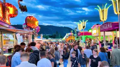Besucher gehen zwischen beleuchteten Fahrgeschäften und Buden über den St. Veiter Wiesenmarkt.