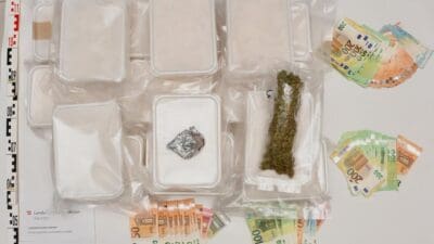 Sichergestellte Drogen in Plastikboxen, Cannabis und Bargeld auf einem Tisch mit Messskala