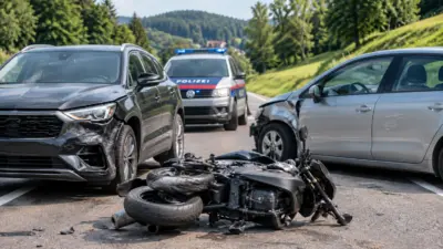 Beschädigte Pkw und ein Motorrad auf der Straße nach einer Kollision mit einem Polizeifahrzeug im Hintergrund.