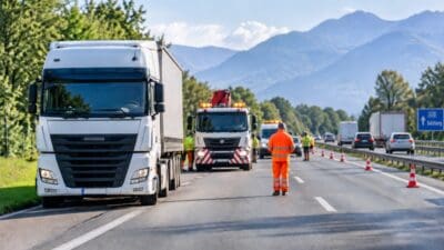 Einsatzkräfte in Warnkleidung bei einer Verkehrskontrolle auf der Alpenautobahn mit Lkw und Bergen im Hintergrund