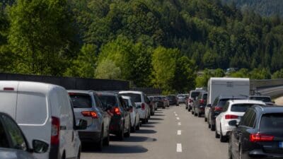 Lange Kolonne von Autos und Lieferwagen im Stau auf einer Autobahn vor bewaldeten Hügeln