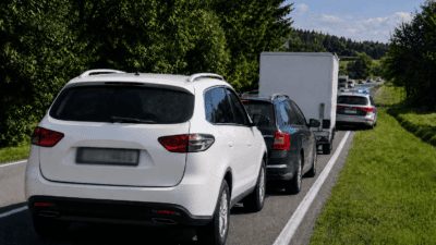 Weißer SUV und weitere Fahrzeuge warten in einer Kolonne hinter einem Polizeiauto mit Blaulicht.