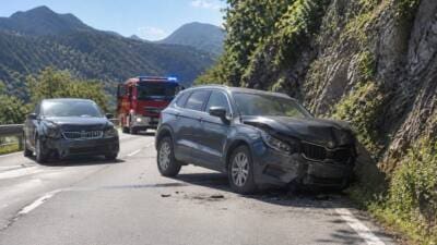Zwei stark beschädigte Pkw nach einem Frontalunfall auf einer Bergstraße mit einem Feuerwehrfahrzeug im Hintergrund