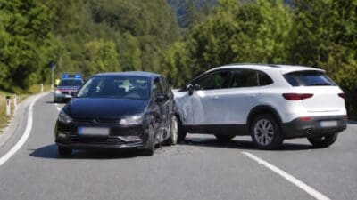 Ein schwarzer und ein weißer Pkw nach einer Kollision auf einer Bergstraße, Polizeiauto im Hintergrund.
