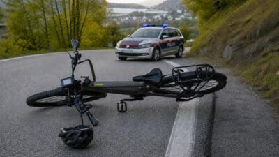 Ein umgestürztes E-Bike liegt auf der Straße neben einem Helm vor einem Polizeiwagen mit Blaulicht.