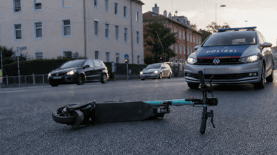 Ein umgestürzter E-Scooter liegt auf der Fahrbahn vor einem Polizeifahrzeug.