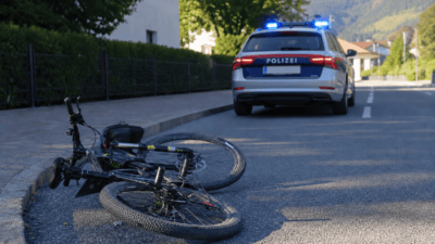 Ein umgestürztes Fahrrad liegt am Straßenrand vor einem Polizeiwagen mit Blaulicht.
