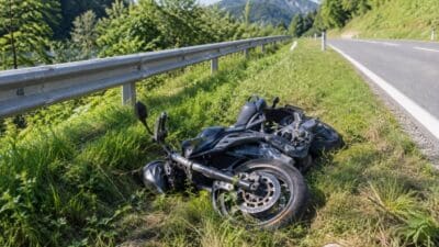 Ein verunglücktes Motorrad liegt im Gras neben einer Leitplanke an der Straße.