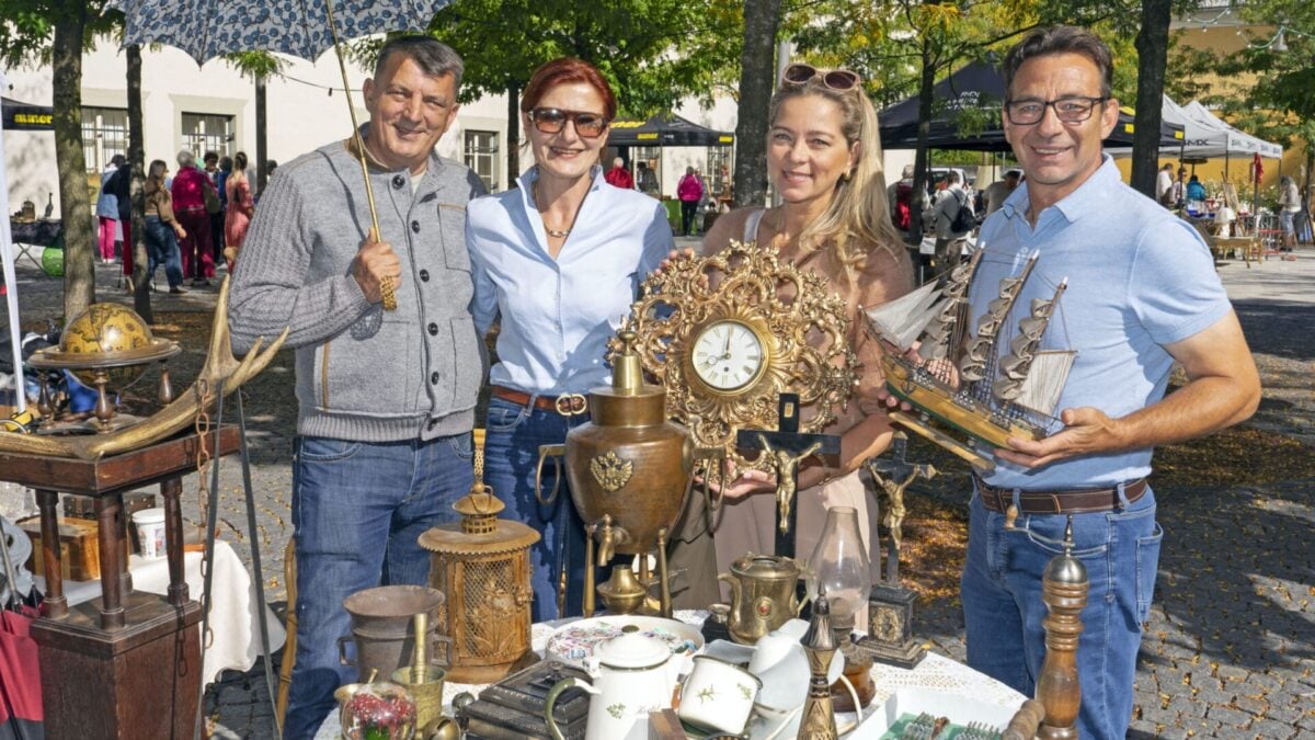Vier Erwachsene stehen hinter einem Tisch mit Antiquitaeten auf einem Flohmarkt.
