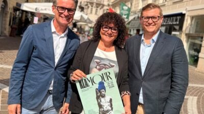 Drei Personen halten in der Klagenfurter Innenstadt ein Plakat für das Einkaufsfestival KLAMOUR.