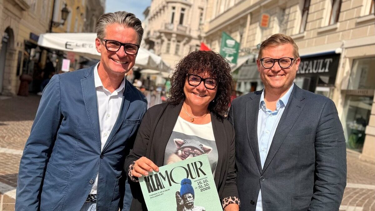 Drei Personen halten in der Klagenfurter Innenstadt ein Plakat für das Einkaufsfestival KLAMOUR.