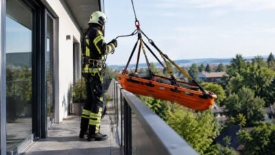 Ein Feuerwehrmann seilt eine Korbschleiftrage von der Terrasse eines Wohnhauses ab.