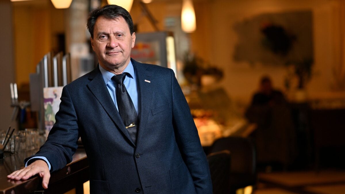 Ein Mann mittleren Alters in einem dunklen Anzug mit Krawatte steht an einer Theke.