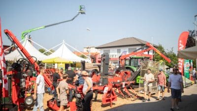 Mehrere Besucher stehen vor roten Holzverarbeitungsmaschinen auf dem Gelände der Holzmesse Klagenfurt.