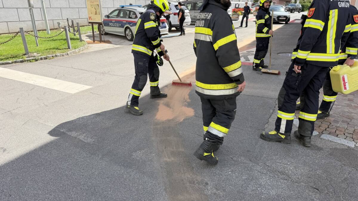 Feuerwehrleute in Schutzkleidung binden eine Ölspur auf der Straße mit einem Besen