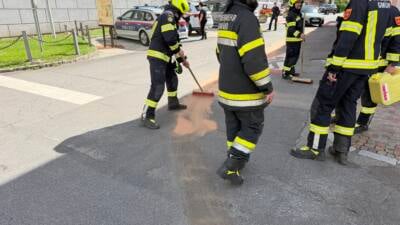 Feuerwehrleute in Schutzkleidung binden eine Ölspur auf der Straße mit einem Besen