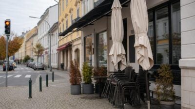Vor einem Kaffeehaus an einer Straße stehen geschlossene Sonnenschirme und gestapelte Stühle auf dem Gehsteig.