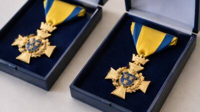 Goldene Ehrenzeichen mit blau-gelben Bändern liegen in geöffneten Präsentationsetuis.