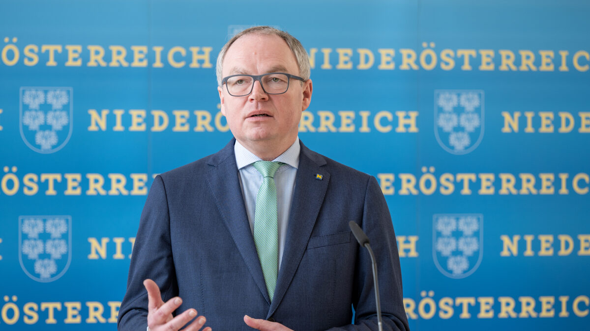 Ein Mann mit Brille in einem dunklen Anzug und grüner Krawatte gestikuliert an einem Rednerpult.