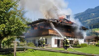 Feuerwehrleute löschen mit einem Schlauch ein brennendes Bauernhaus mit starker Rauchentwicklung.