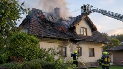 Feuerwehrleute bekämpfen mit einer Drehleiter einen Brand im Dach eines Wohnhauses