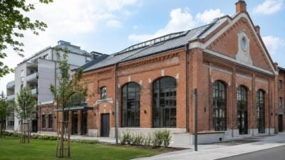 Renoviertes rotes Backsteingebäude mit großen Bogenfenstern und Glasdach vor grüner Wiese in Ottakring