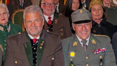 Sitzende Teilnehmer einer Gedenkveranstaltung, darunter Männer in Uniform und traditioneller Kleidung