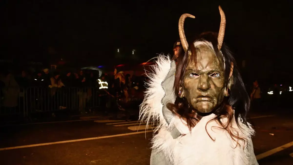 Krampusfigur mit Hörnern und hellem Fellkostüm bei einem nächtlichen Umzug