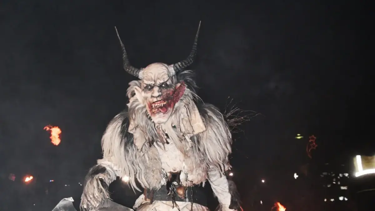 Eine gehörnte Krampusfigur in zotteligem Kostüm hält nachts eine brennende Fackel.