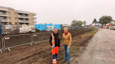Zwei Personen stehen an einer abgesperrten, schlammigen Straßenbaustelle.
