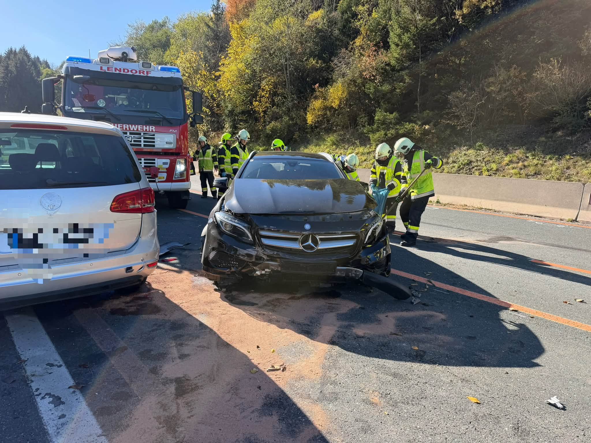 Feuerwehrleute stehen neben einem beschädigten Pkw und einem Feuerwehrfahrzeug auf der Straße.