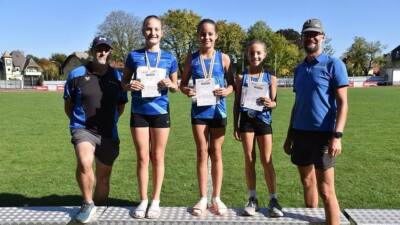 Drei junge Leichtathletinnen mit Urkunden und Medaillen auf einem Podest