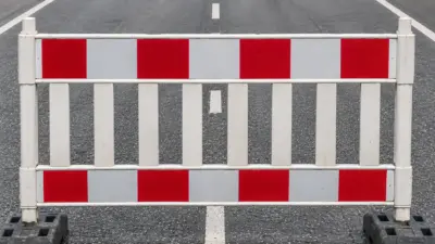 Rot-weiße Straßensperre quer über einer asphaltierten Fahrbahn mit Mittellinie.