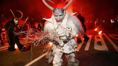 Maskierter Krampus mit Hörnern und Reisigbündel auf einer nächtlichen Straße