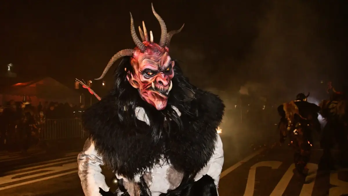 Ein Krampus mit Hörnermaske und schwarzem Fell steht nachts auf einer Straße.