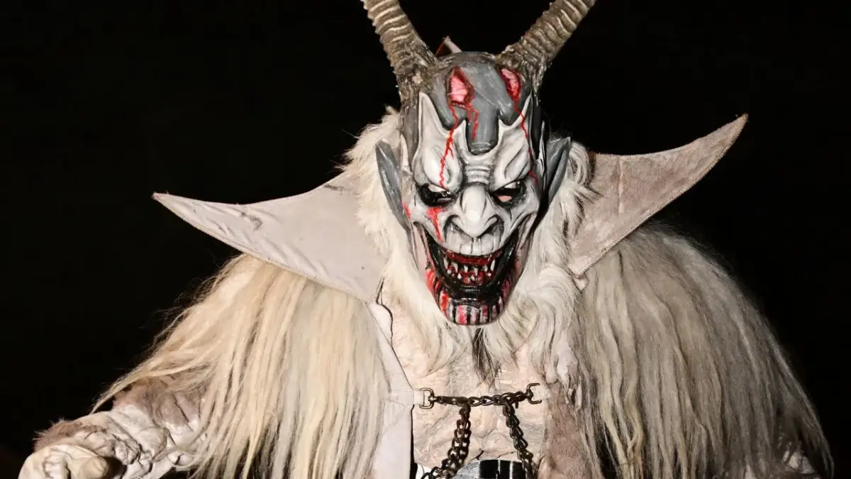 Eine Krampusfigur mit langen Hörnern und zotteligem hellem Kostüm auf einer nächtlichen Straße.