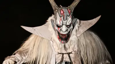 Eine Krampusfigur mit langen Hörnern und zotteligem hellem Kostüm auf einer nächtlichen Straße.