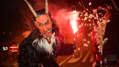 Krampus mit Hörnermaske und Fellkostüm vor leuchtenden Funken