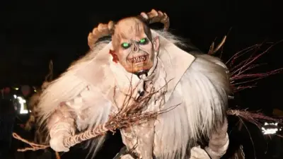 Eine Krampusfigur mit Hörnermaske, weißem Fellkostüm und Ästen in der Hand.