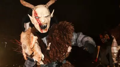 Eine Krampusfigur trägt eine gehörnte Maske und ein zotteliges Fellkostüm auf einer nächtlichen Straße.