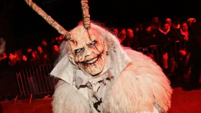 Krampusfigur mit Hörnern und weißem Fellkostüm vor Zuschauern an Absperrgittern